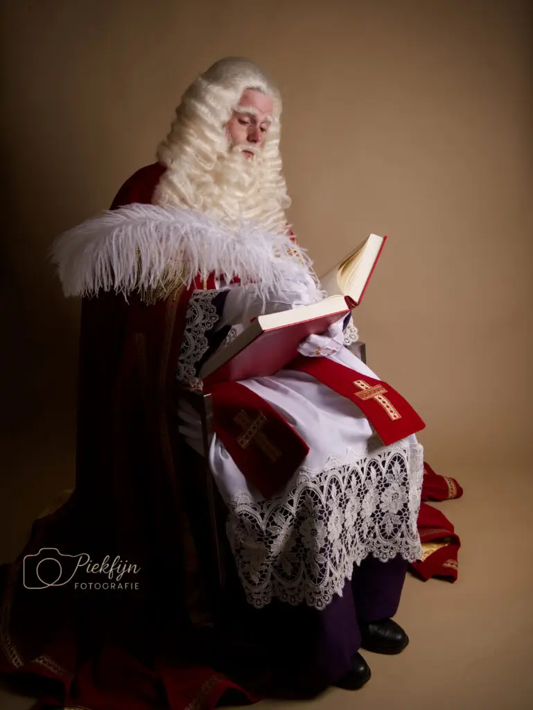 Sinterklaas met boek op schoot, schrijft met een veer.